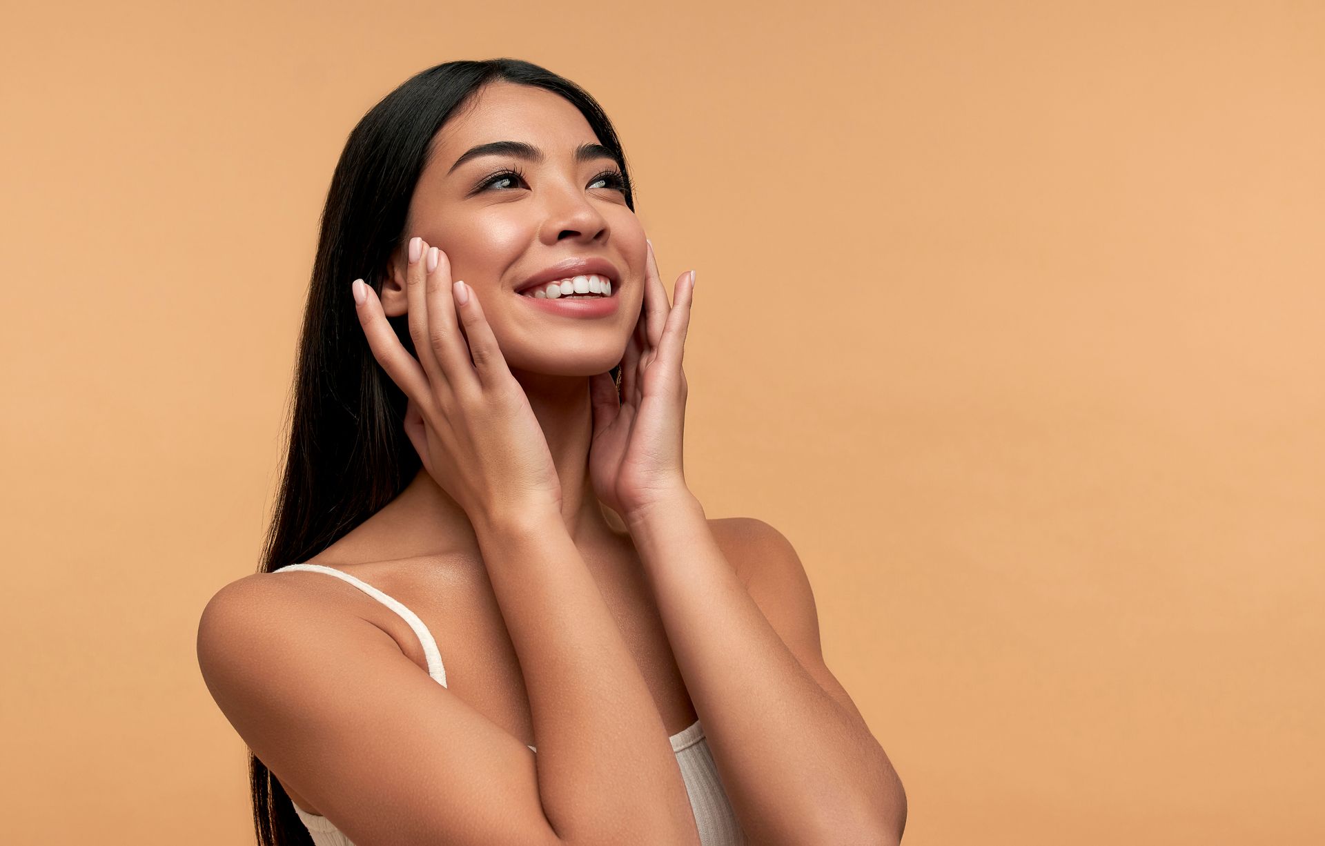 A woman is smiling and touching her face with her hands.