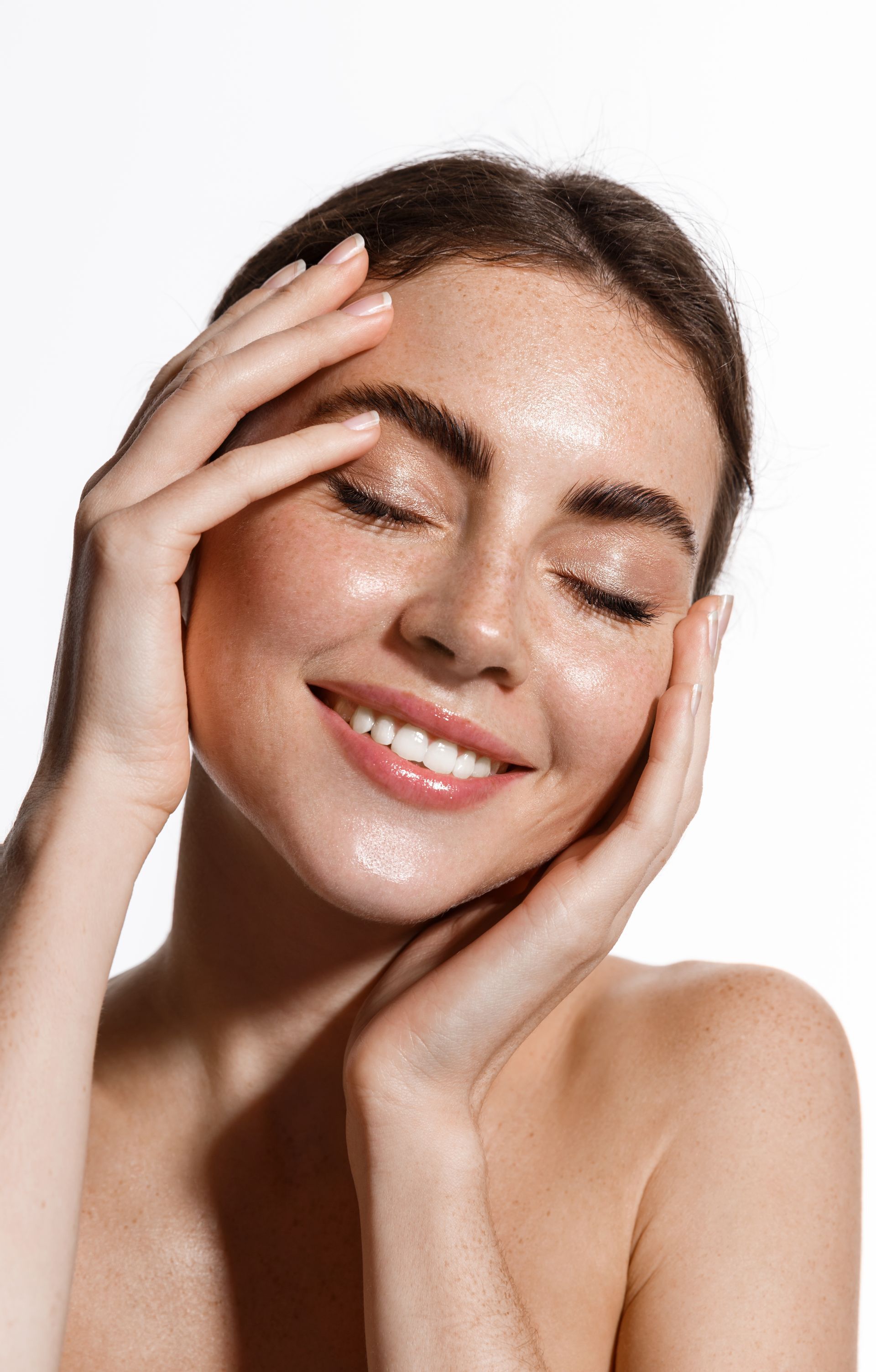 A woman is smiling and touching her face with her hands.