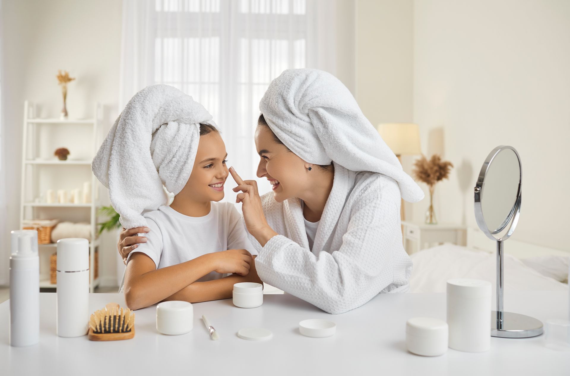 A mother and daughter are sitting at a table with towels wrapped around their heads.