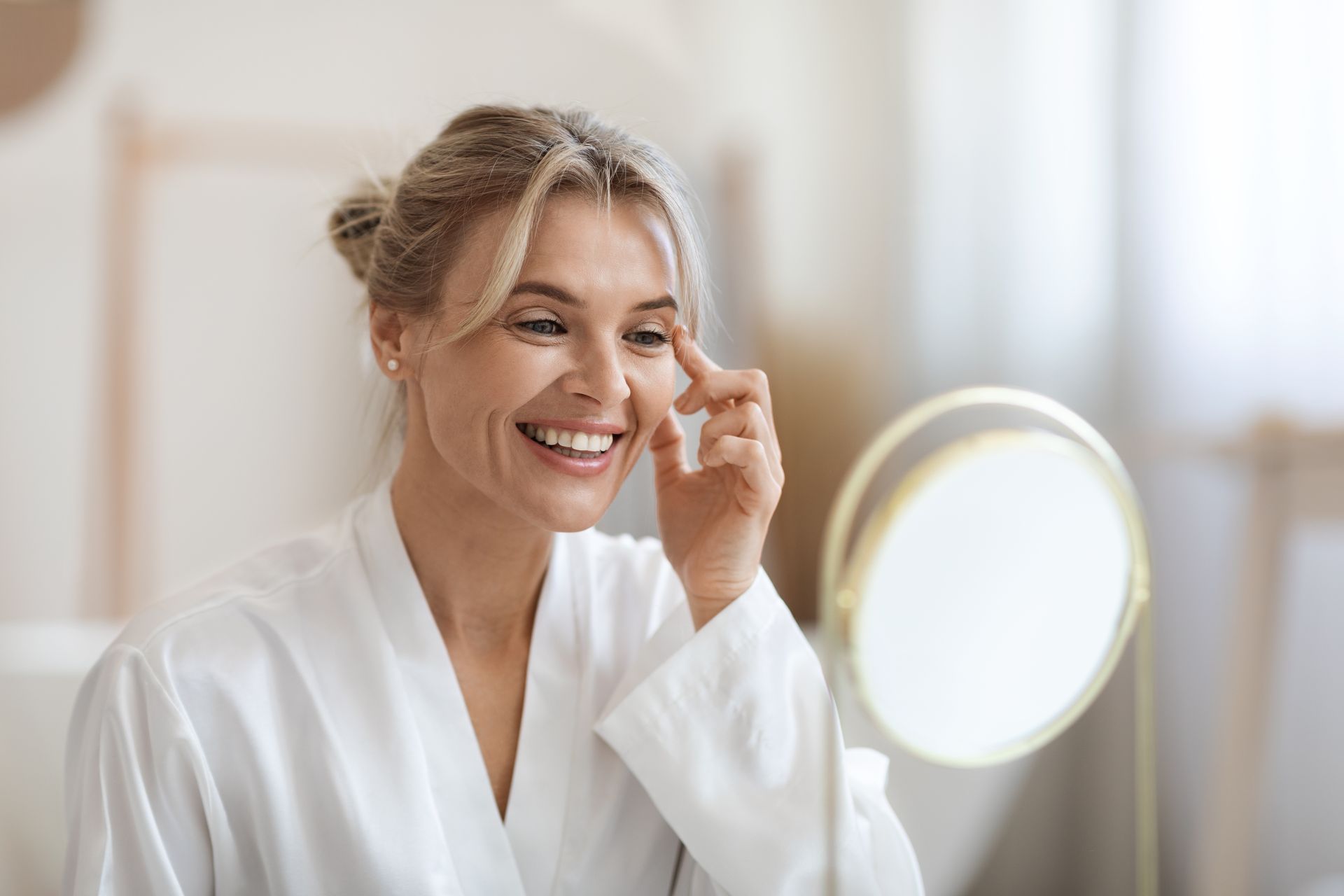 A woman is smiling while looking at her face in a mirror.