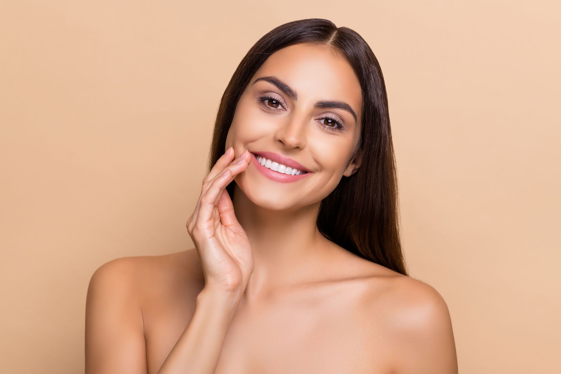 A woman is smiling and touching her face with her hand.