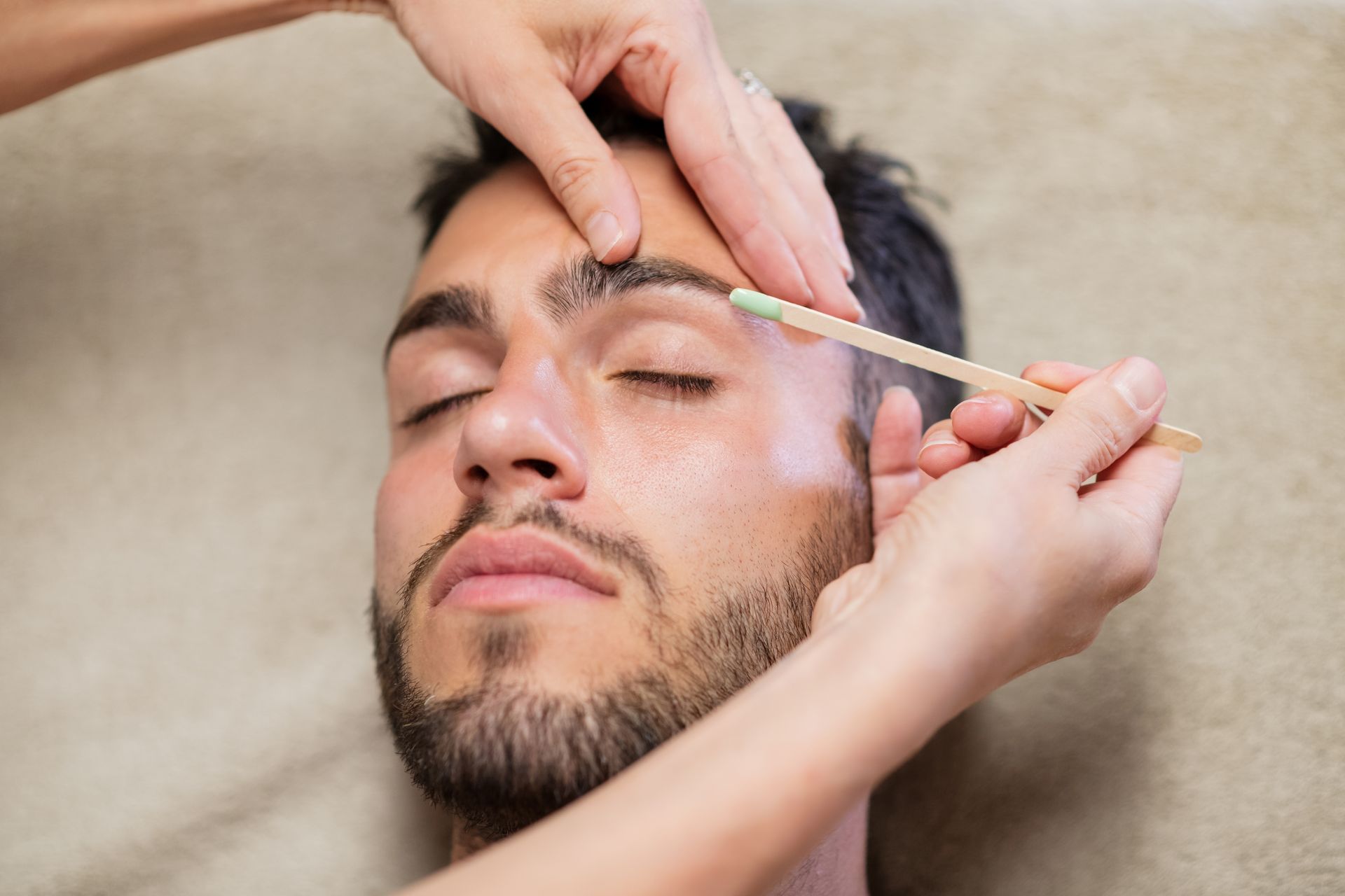 A man is getting his eyebrows waxed by a woman.