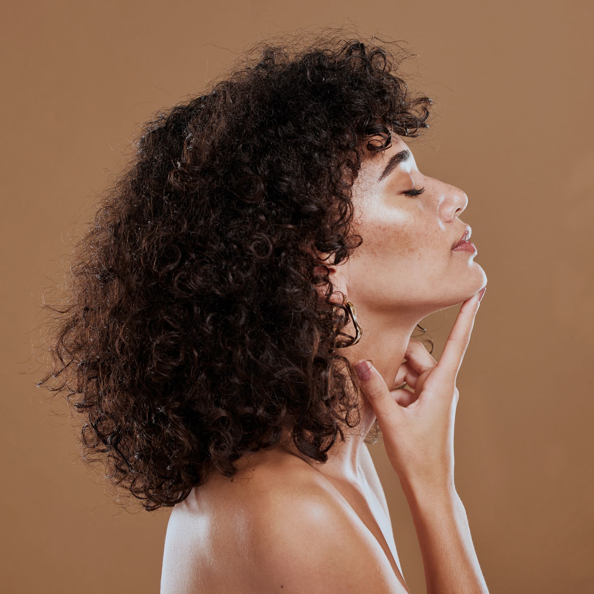 A woman with curly hair is touching her face with her hand.