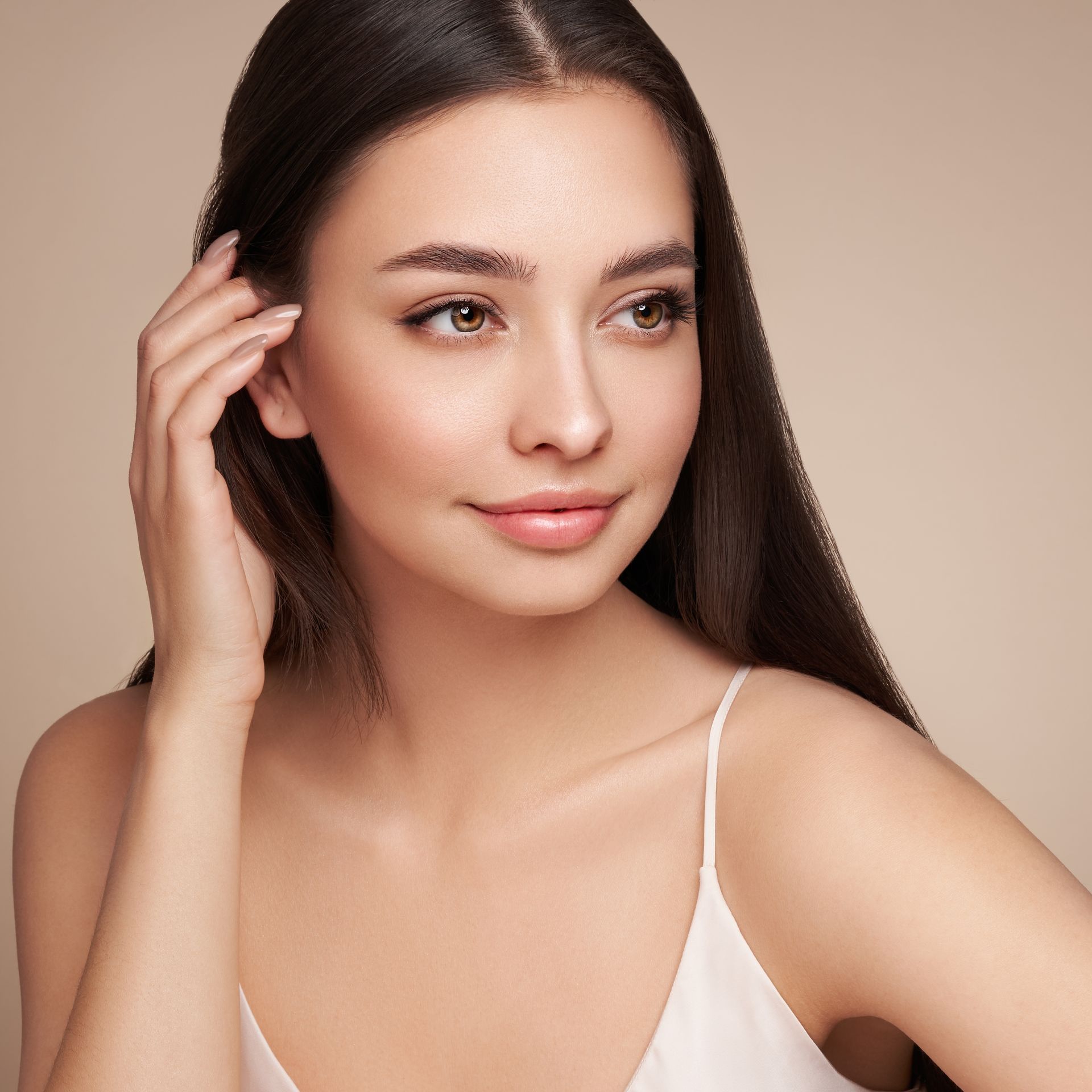 A woman in a white tank top is touching her ear.