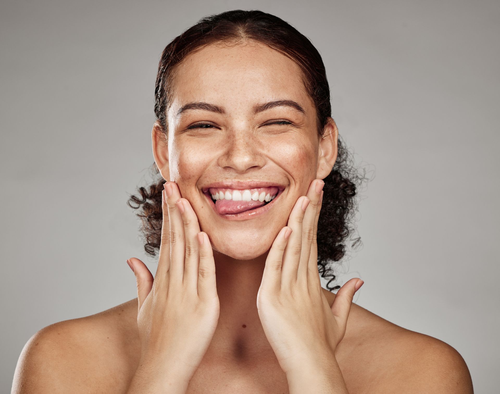 A woman is smiling and touching her face with her hands.