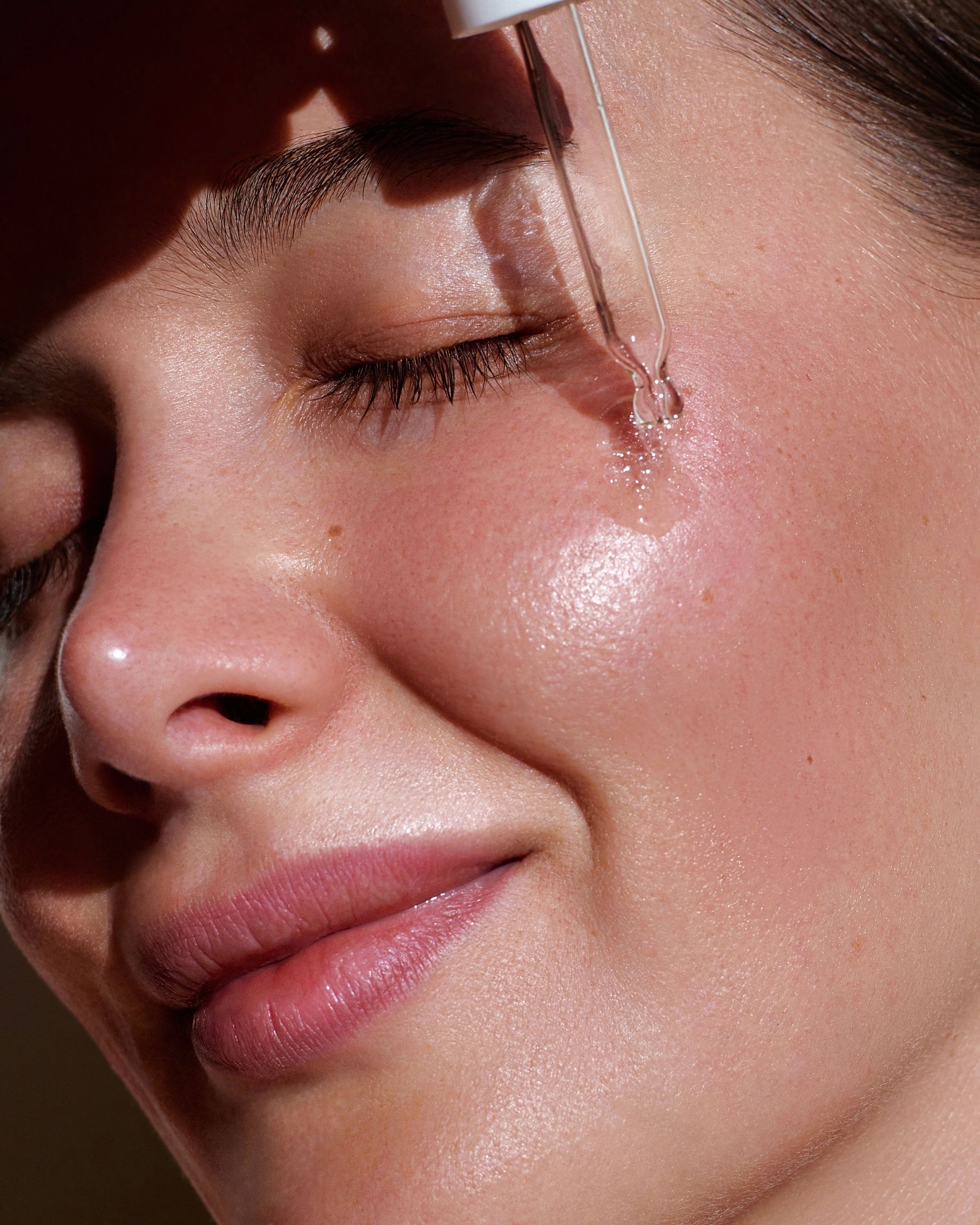 A close up of a woman applying a serum to her face.