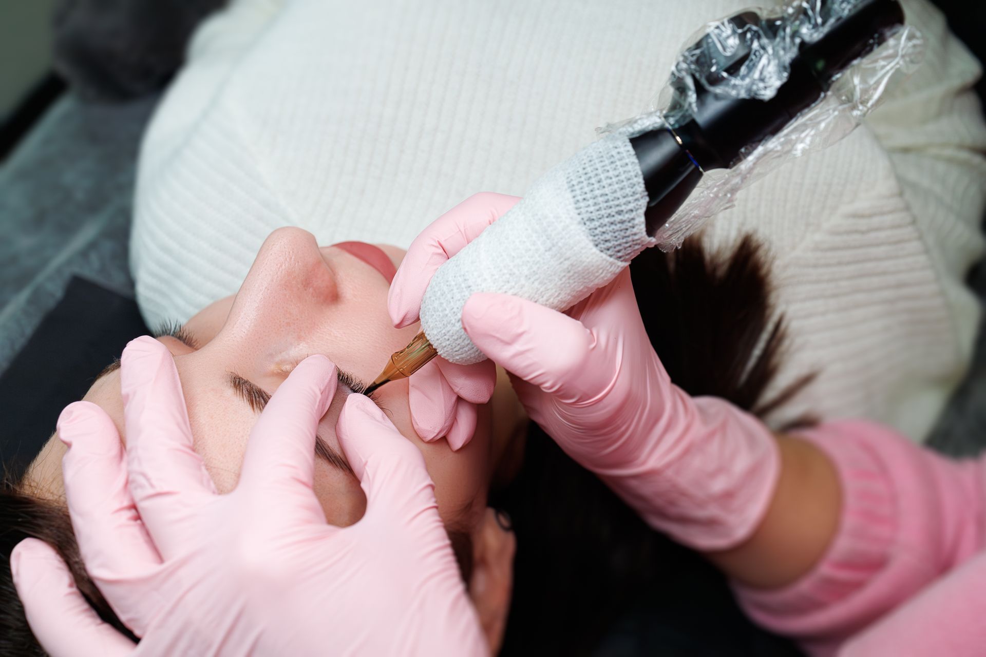 A woman is applying mascara to her eyelashes with a pink brush.