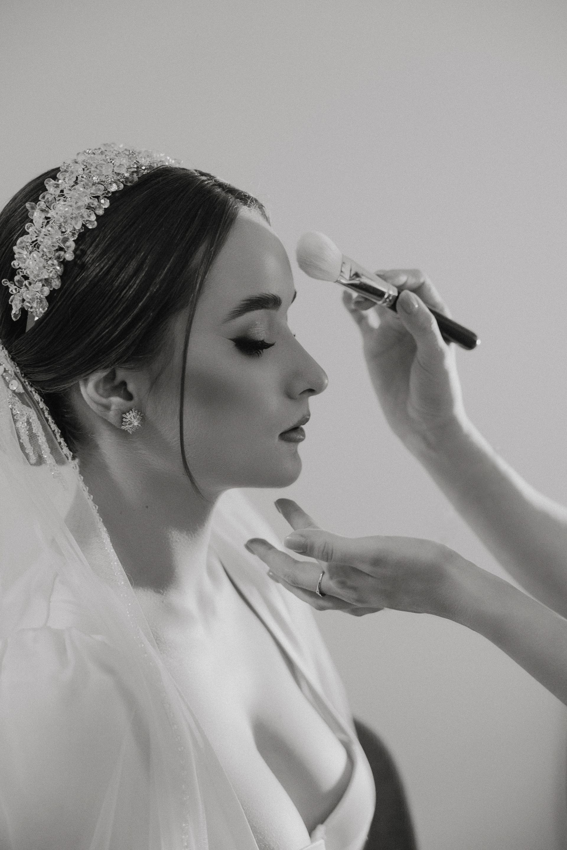 A woman is applying makeup to a bride 's face in a black and white photo.