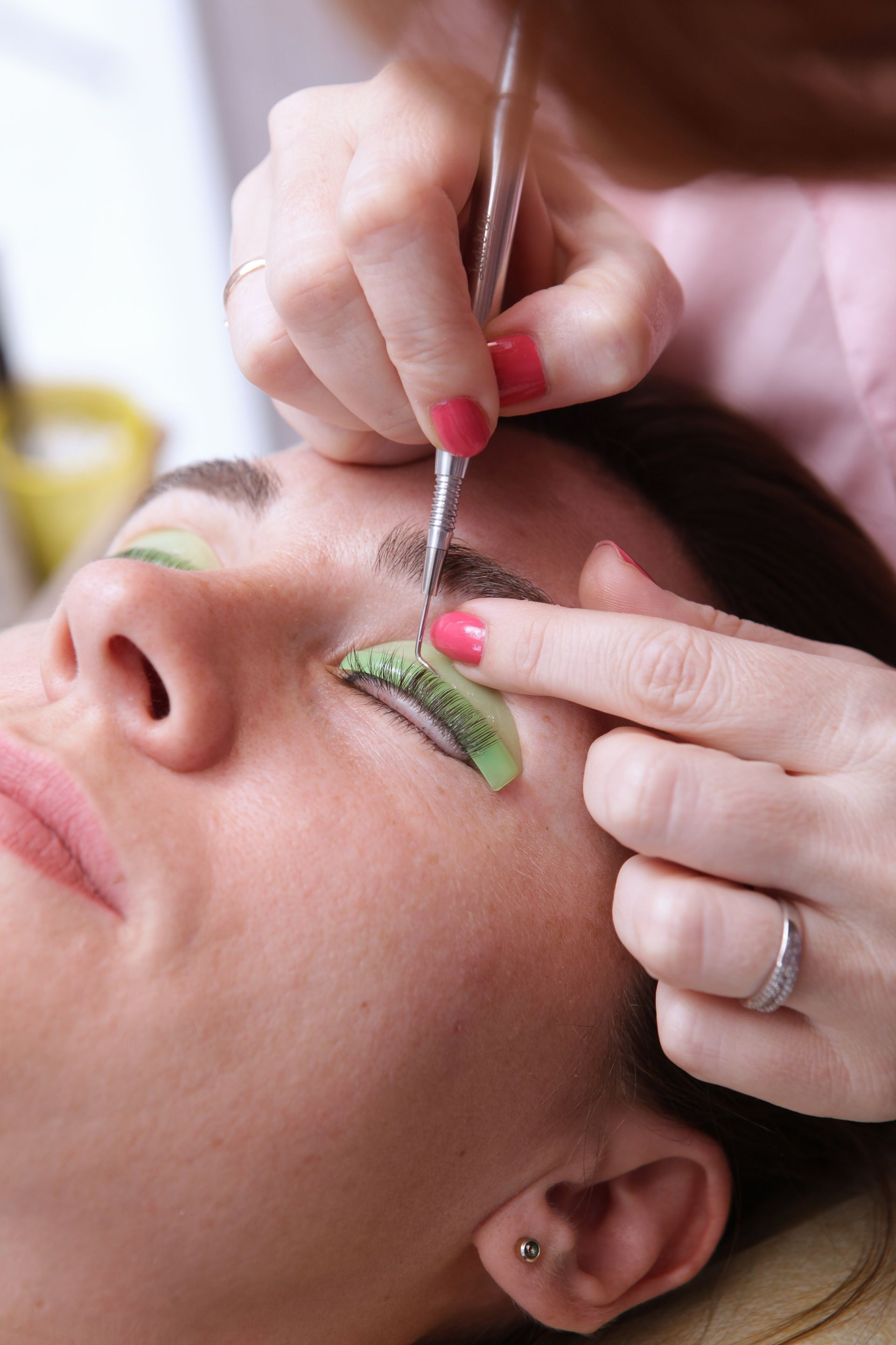 A woman is getting her eyebrows painted green by a makeup artist.