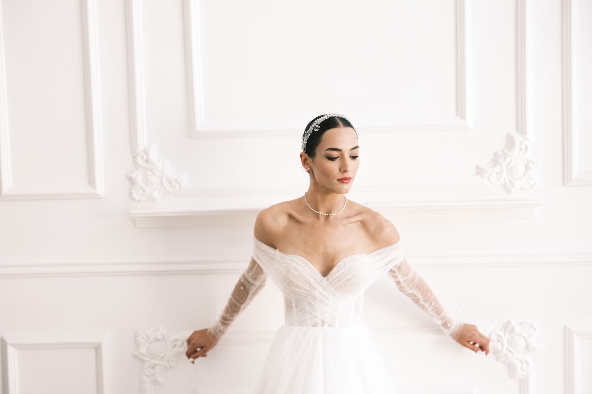 A woman in a wedding dress is standing in front of a white wall.