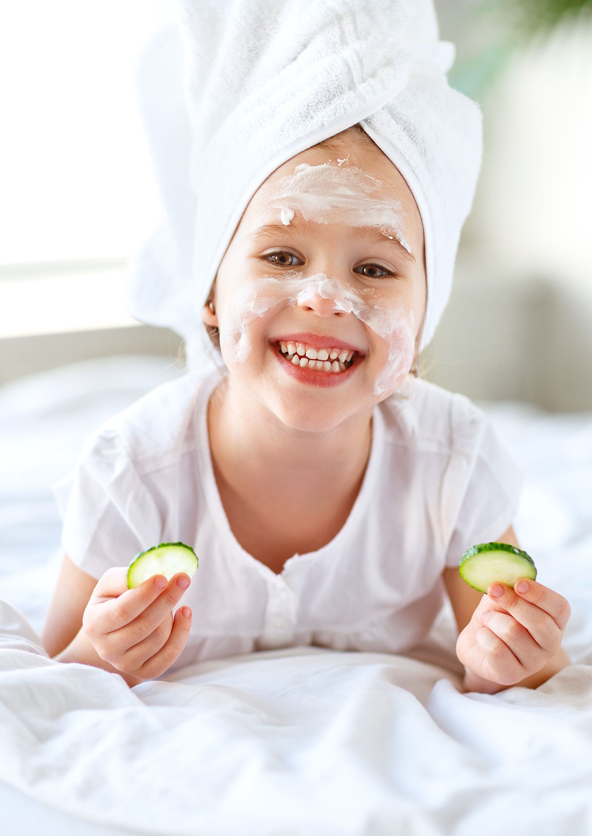 A little girl with a towel wrapped around her head is eating cucumber slices.