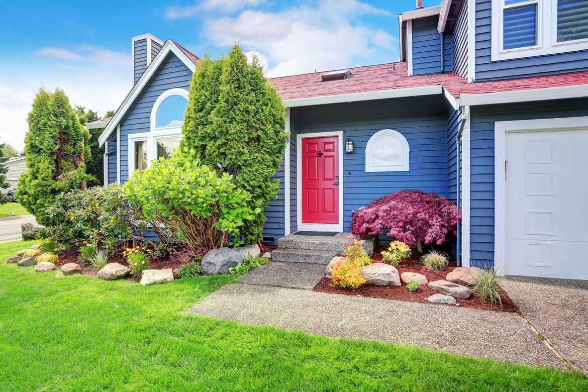 A blue house with a red door and a white garage door.