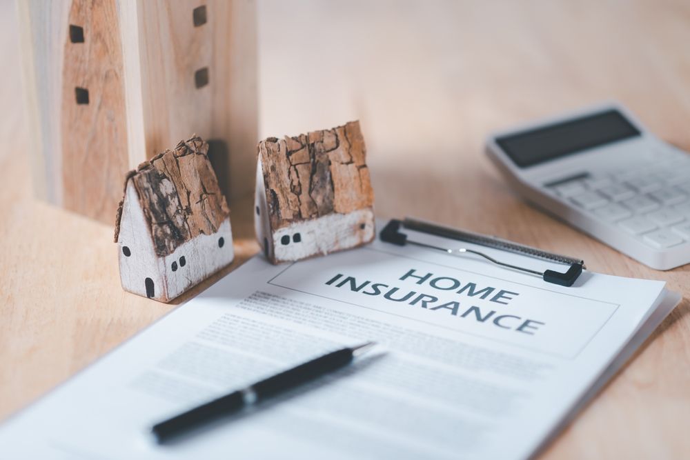 Home insurance document with miniature houses, pen, and calculator on wood.