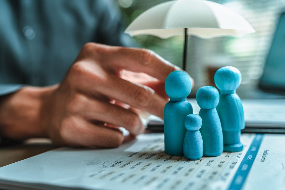 Hand holding a miniature umbrella over a family figurine on a document, symbolizing protection.