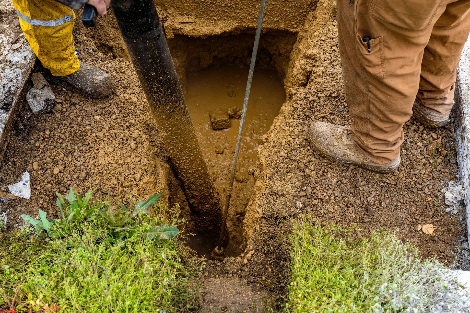 Workers Standing Over a Narrow Trench With a Rope in a Gravel-covered Excavation Site — Fud's Concreting In Airlie Beach, QLD