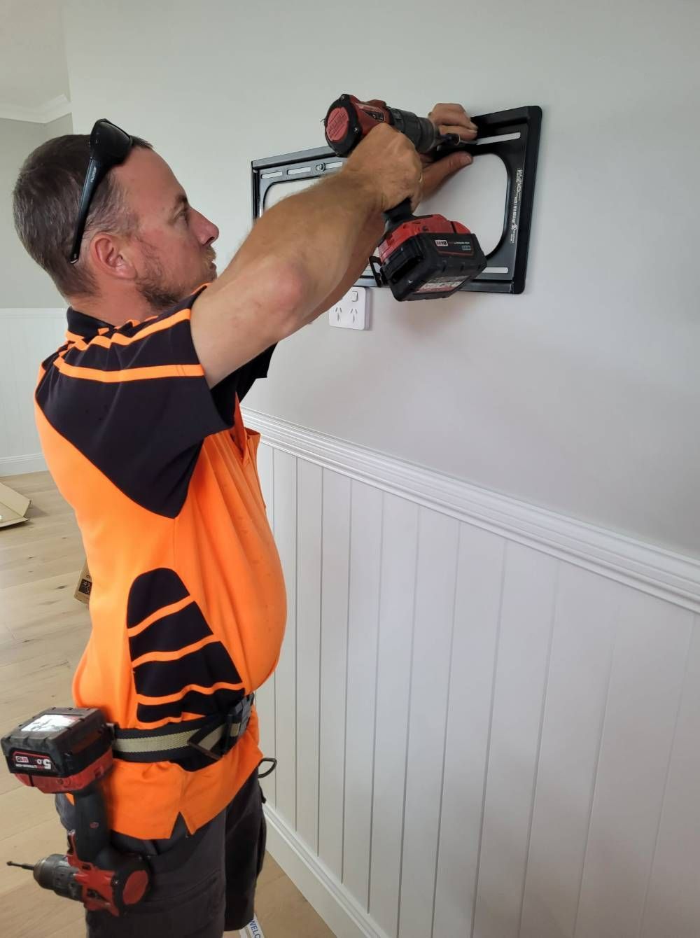 A Man is Using a Drill to Install a Picture Frame on a Wall — Brisbane Antenna Specialists in Brendale, QLD