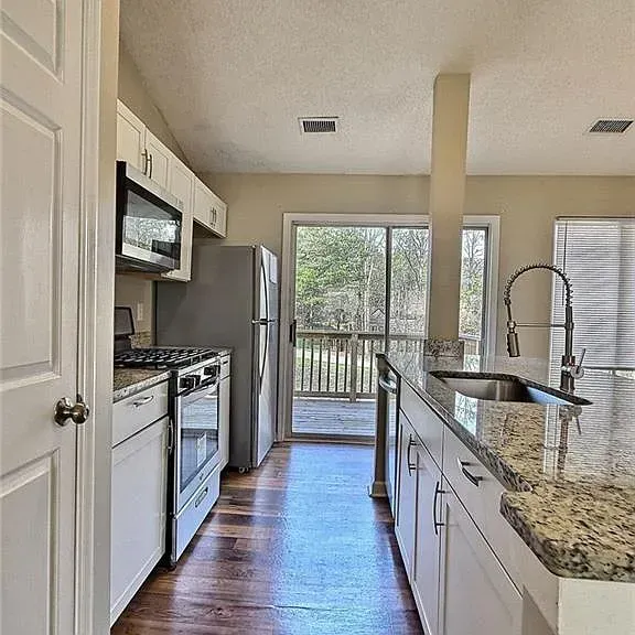 Kitchen with white cabinets, stainless steel appliances, granite countertops, and a sliding glass door to a deck.