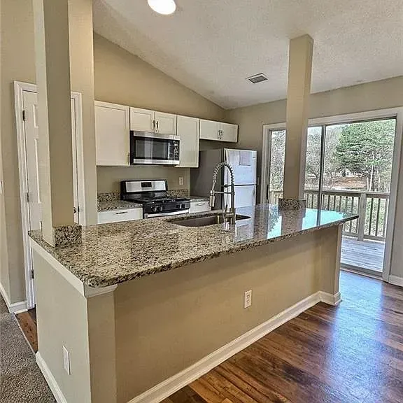 Kitchen with granite countertops, white cabinets, stainless steel appliances, and a sliding glass door to a deck.