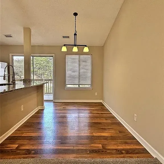 Dining room with wood floors, beige walls, and a hanging light fixture.