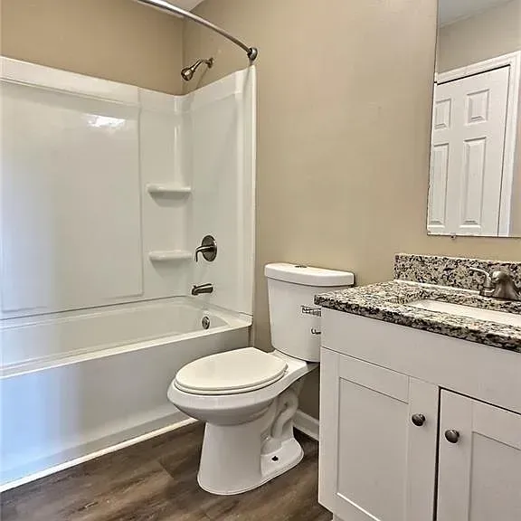 Bathroom with a white tub and toilet, vanity with granite countertop, and beige walls.