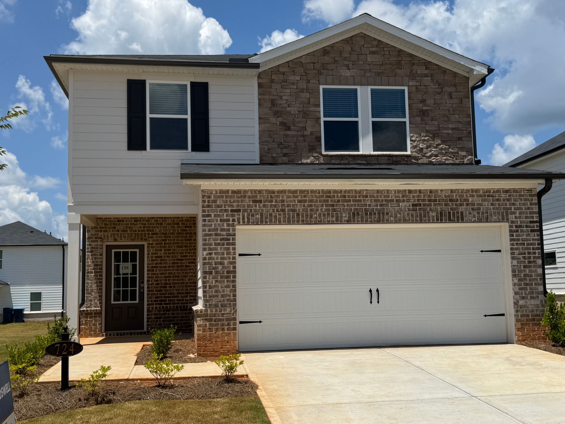 Two-story home with brick and white siding, a two-car garage, and a brown front door under a blue sky.