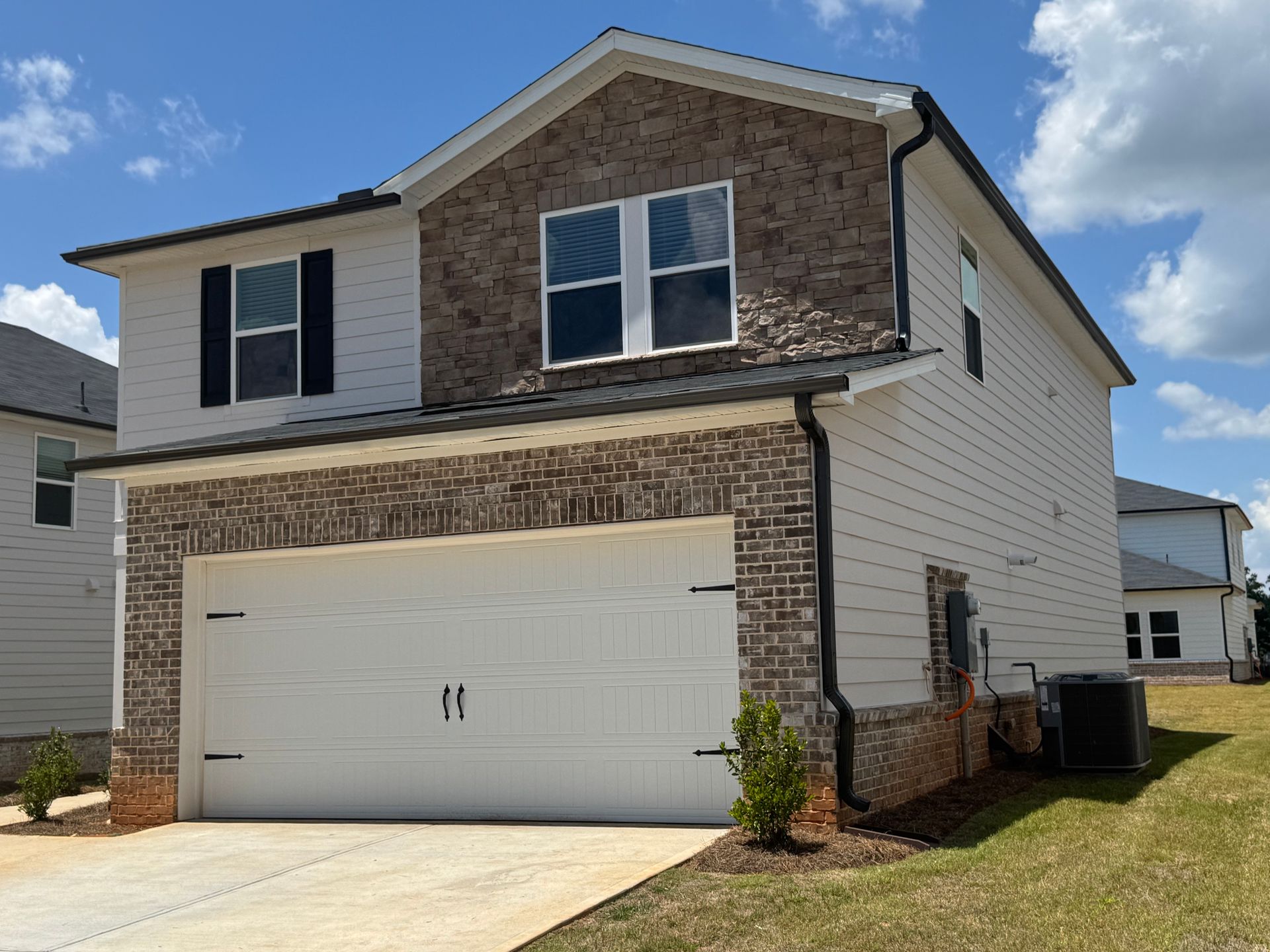 Two-story house with brick and white siding, white garage door, and blue sky.