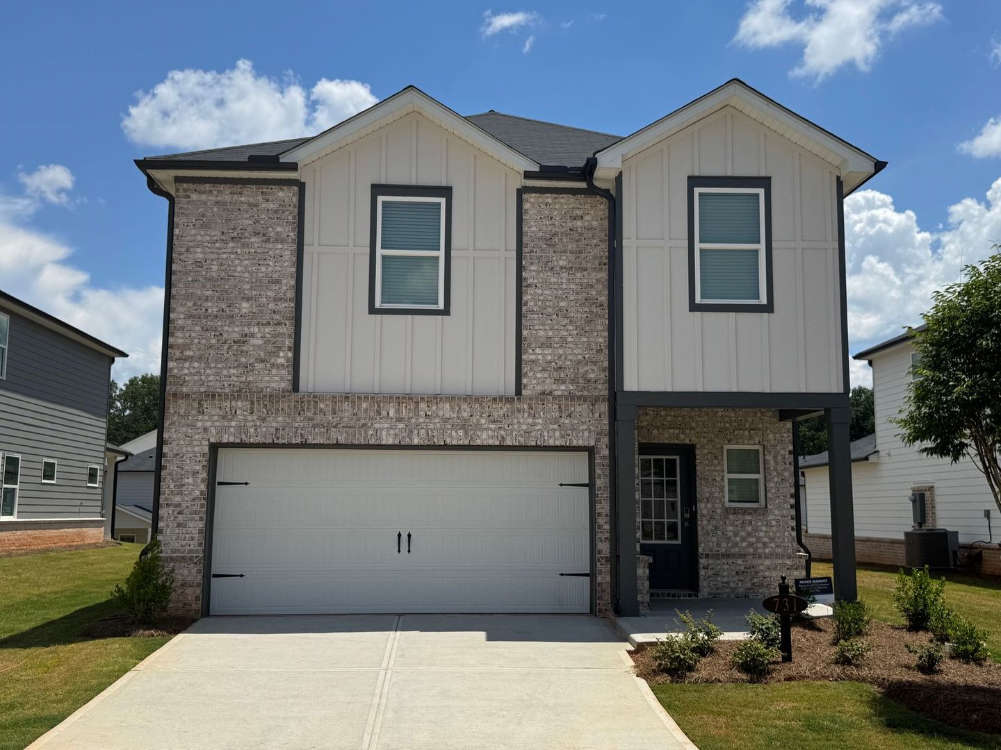 Two-story house with gray brick, white siding, and a two-car garage on a sunny day.