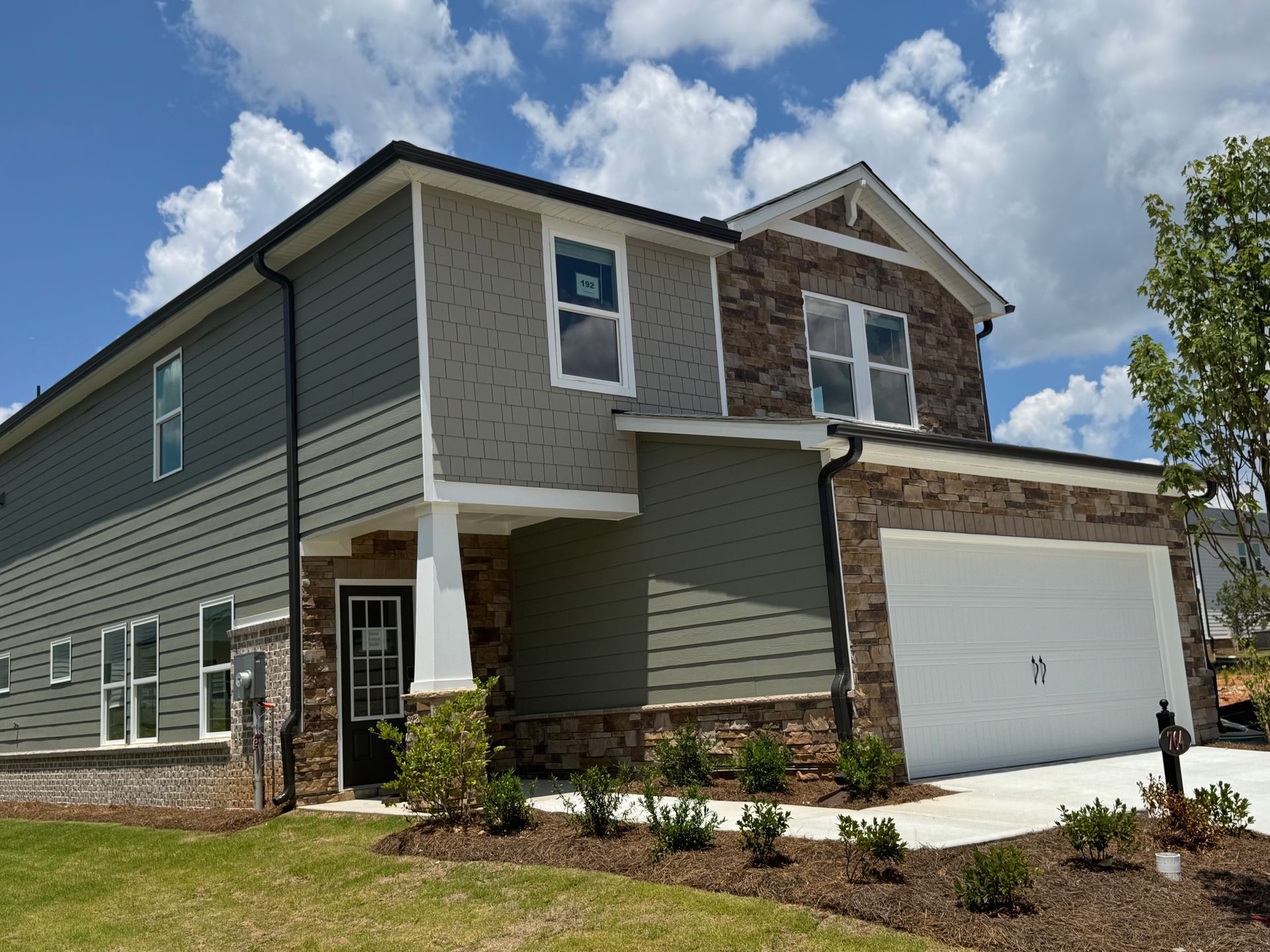Two-story house with gray siding, brick, and a two-car garage on a sunny day.
