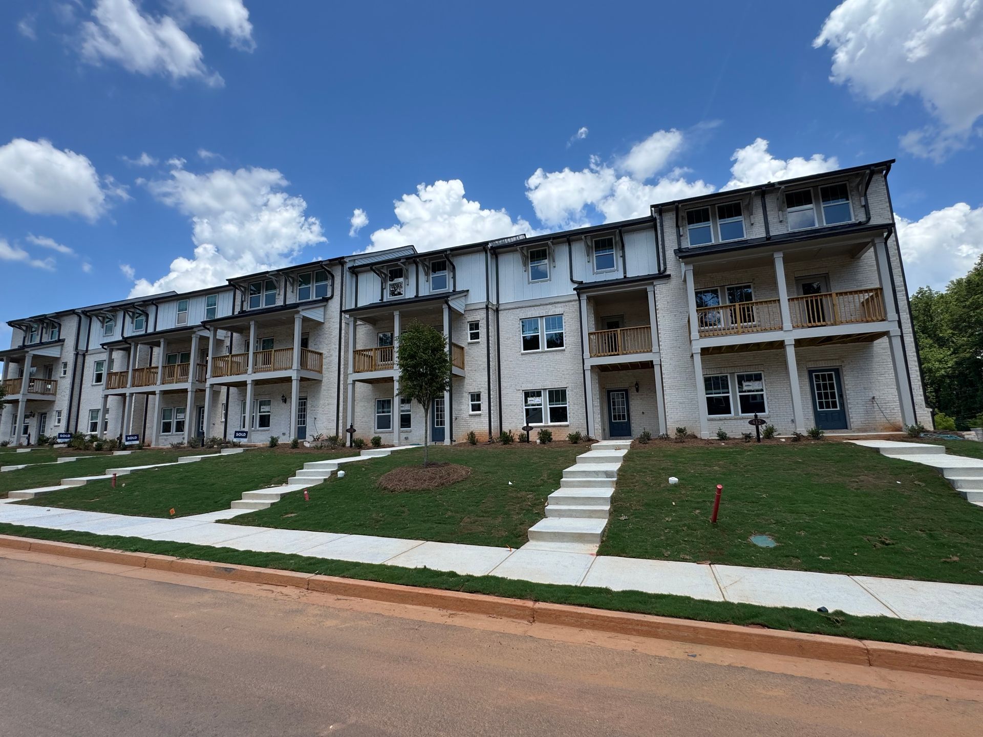 Row of modern white townhomes with balconies and stairs leading to front doors under a blue sky.