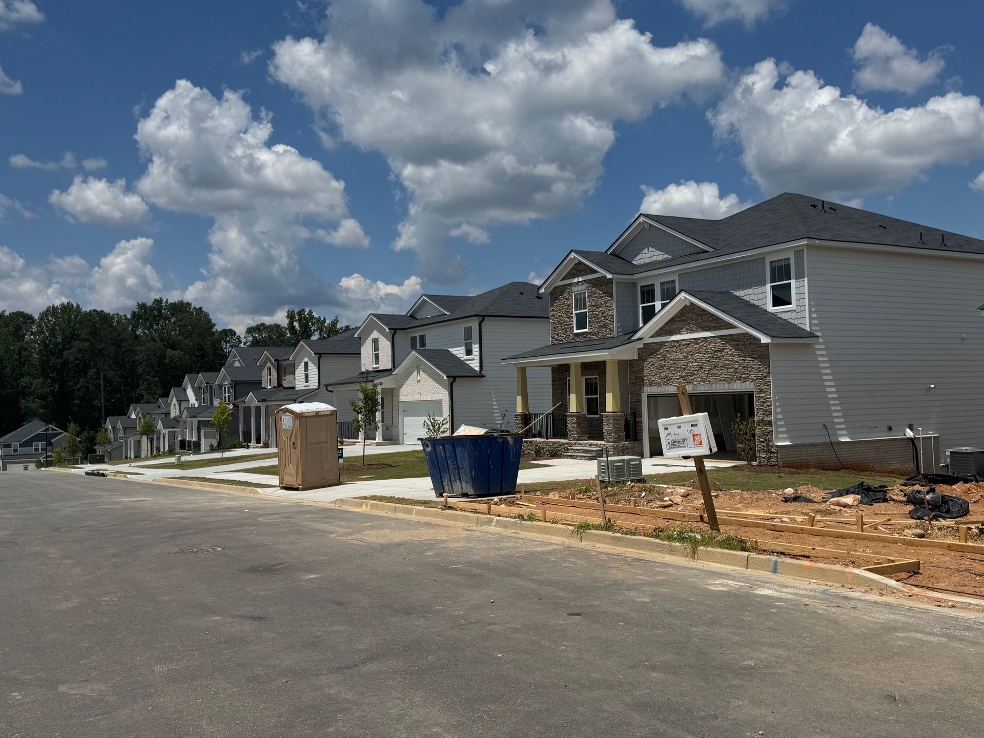 Row of newly built houses under a cloudy blue sky, with construction debris and porta-potty on the street.
