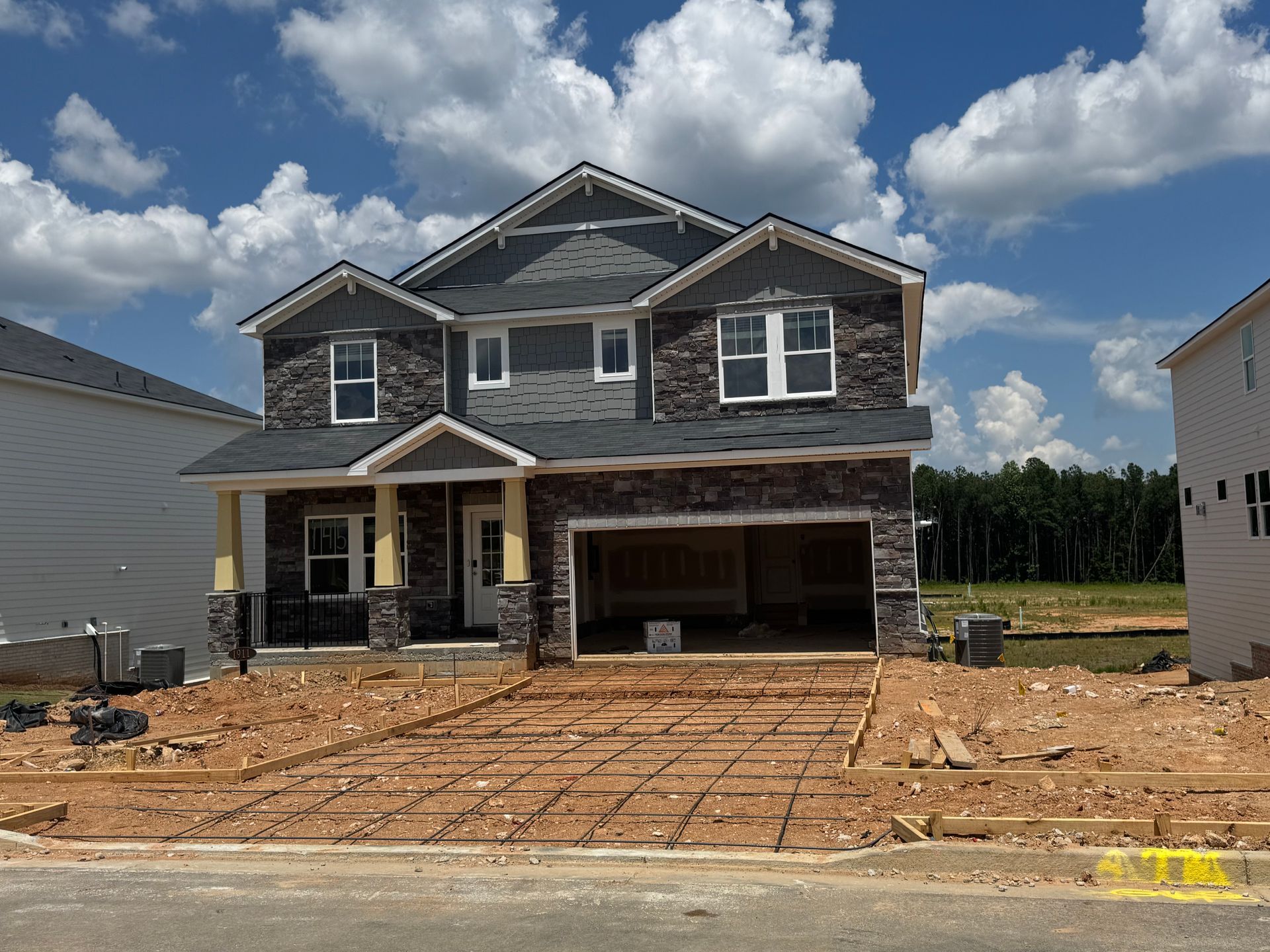 Two-story house under construction; driveway prepped for concrete; blue sky with clouds.