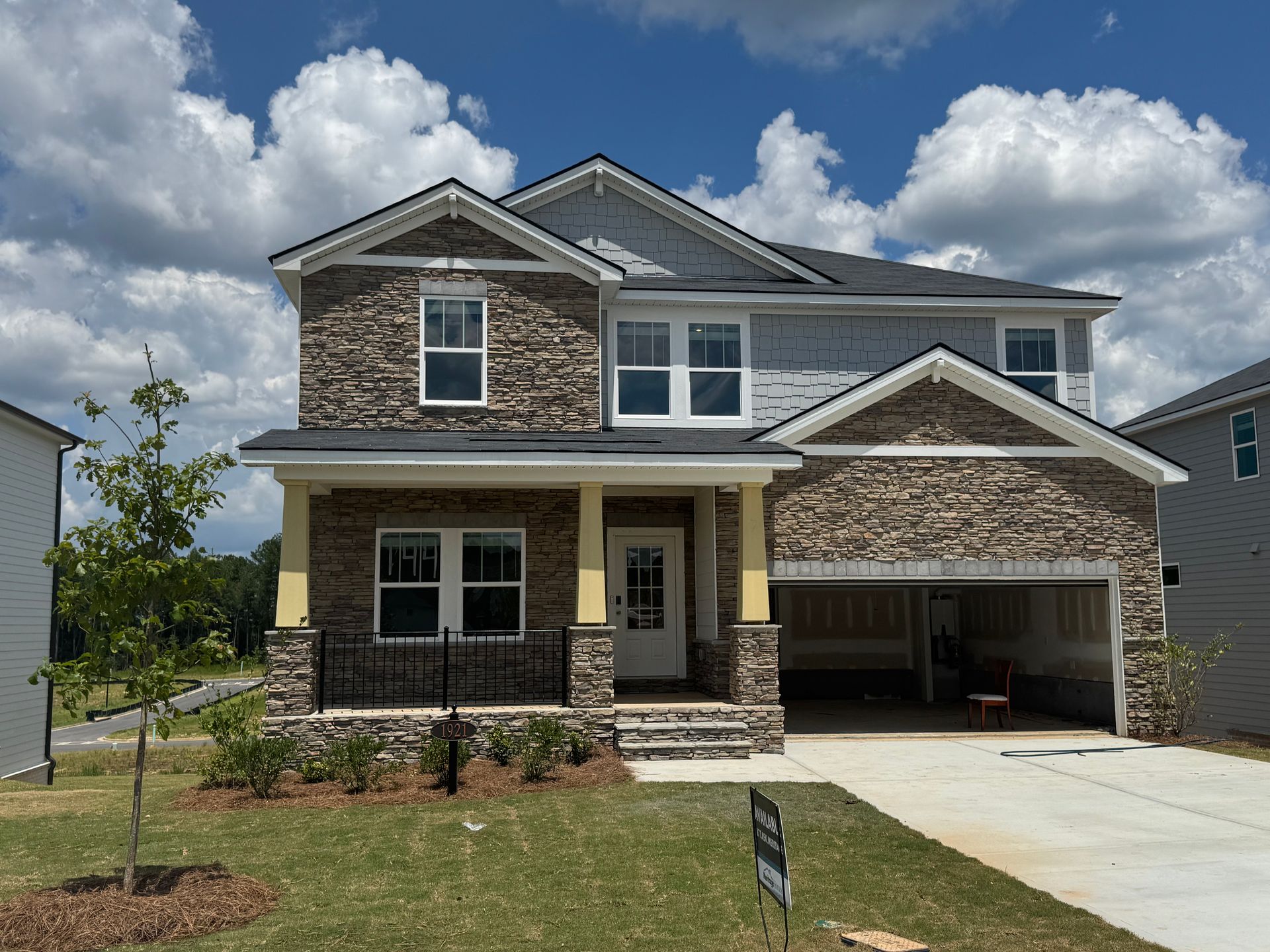 Two-story house with stone and gray siding, a porch, and a garage; sunny day.
