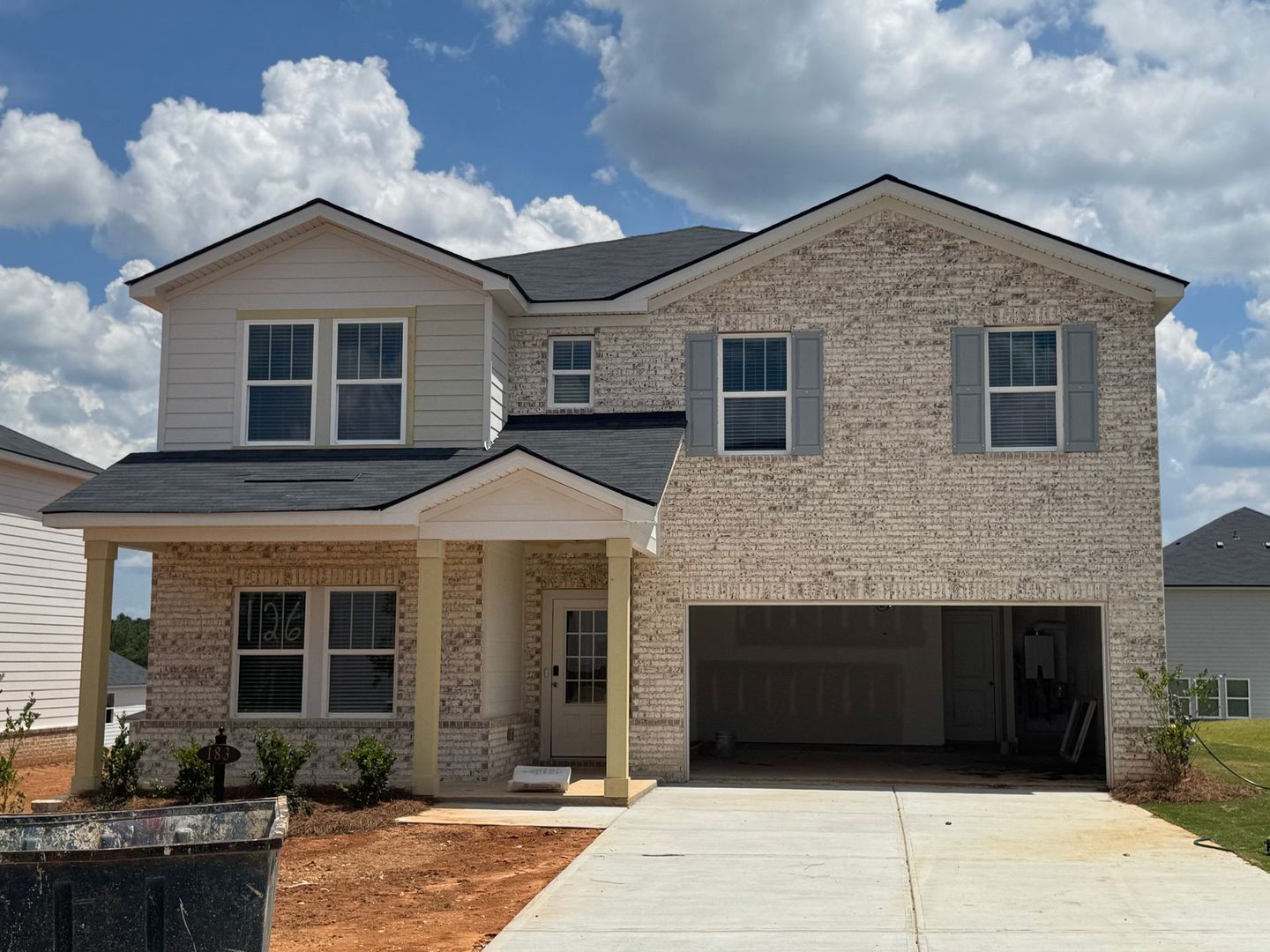 Two-story house with brick facade, garage, and white siding on a sunny day.