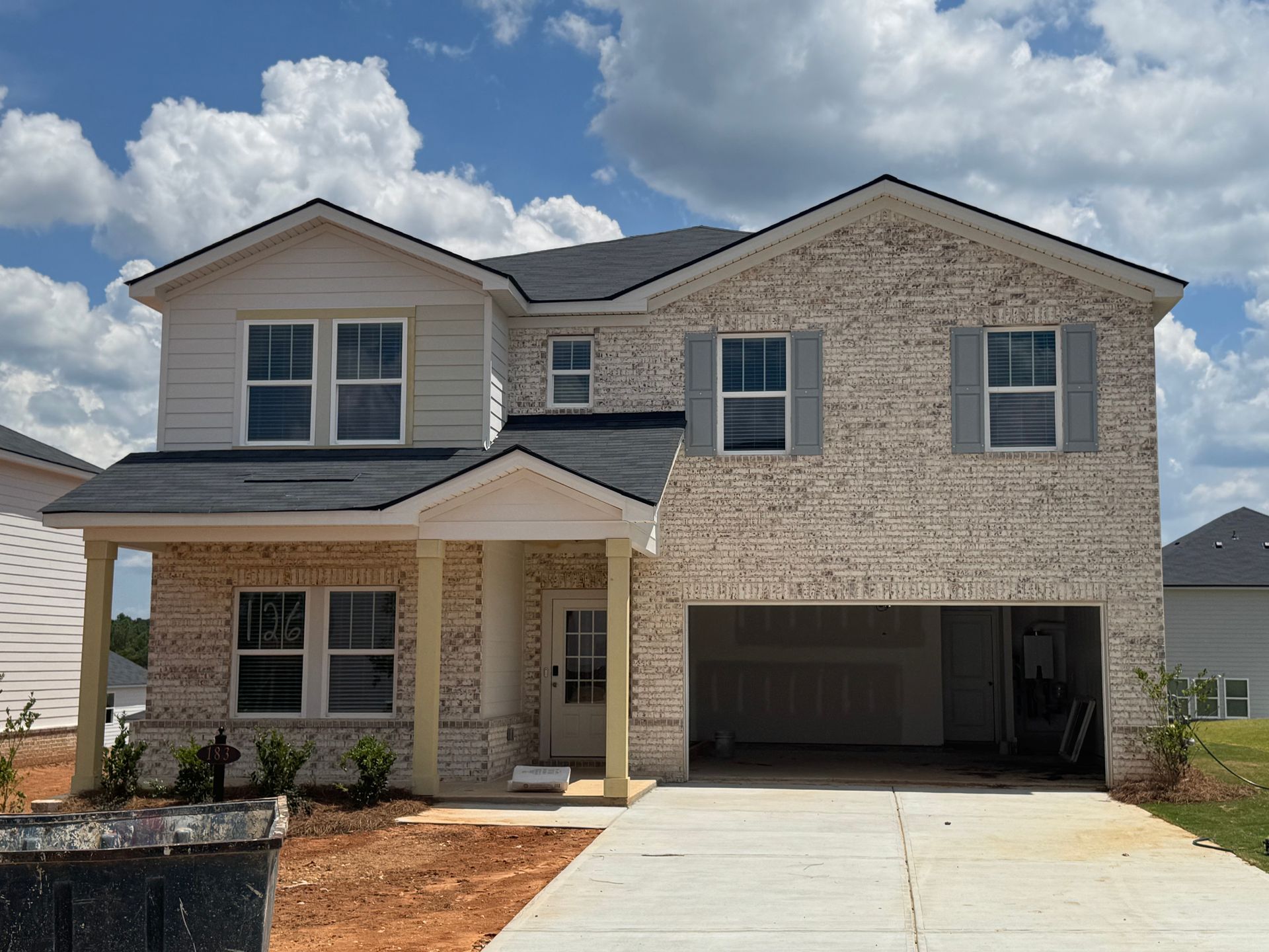 Two-story brick house with an open garage and a concrete driveway under a blue sky.