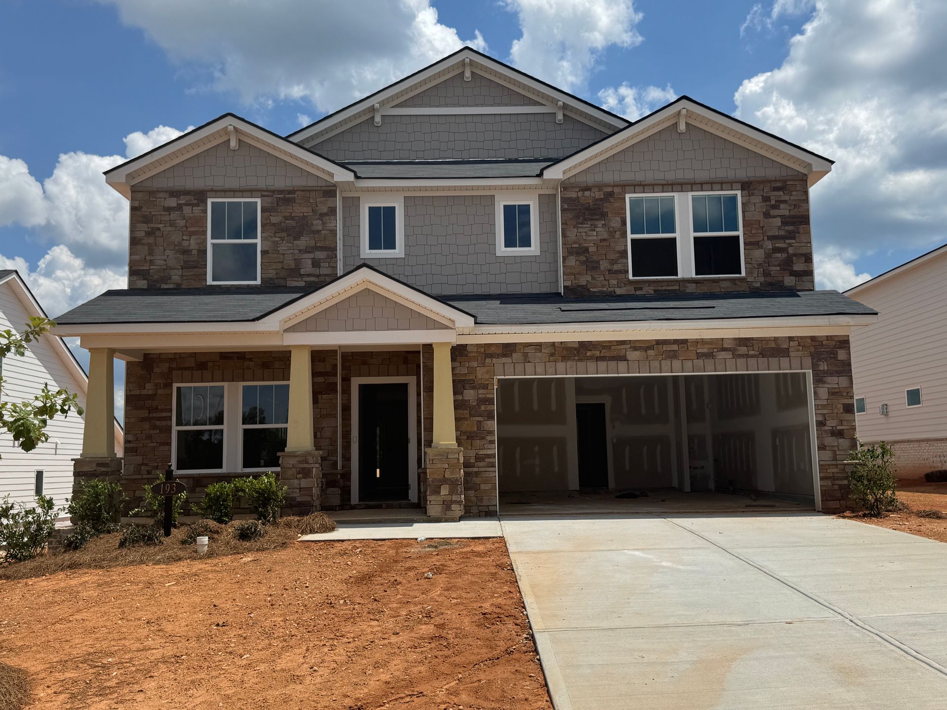 Two-story house with brick, stone, and gray siding, unfinished yard, and a two-car garage.