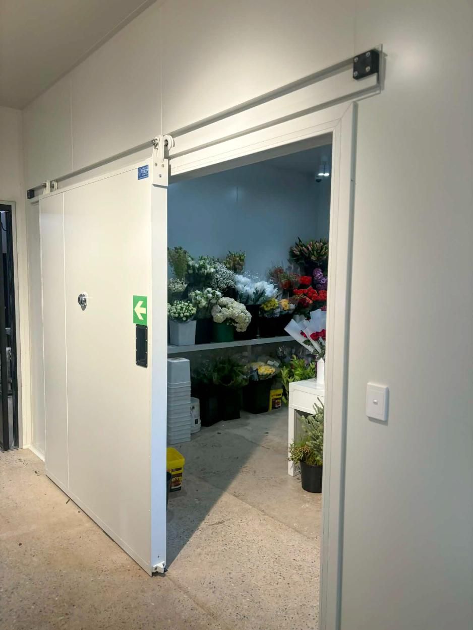 A Sliding White Door is Partially Open, Revealing a Floral Walk-in Refrigerator — Arctic Installations in Winnellie, NT