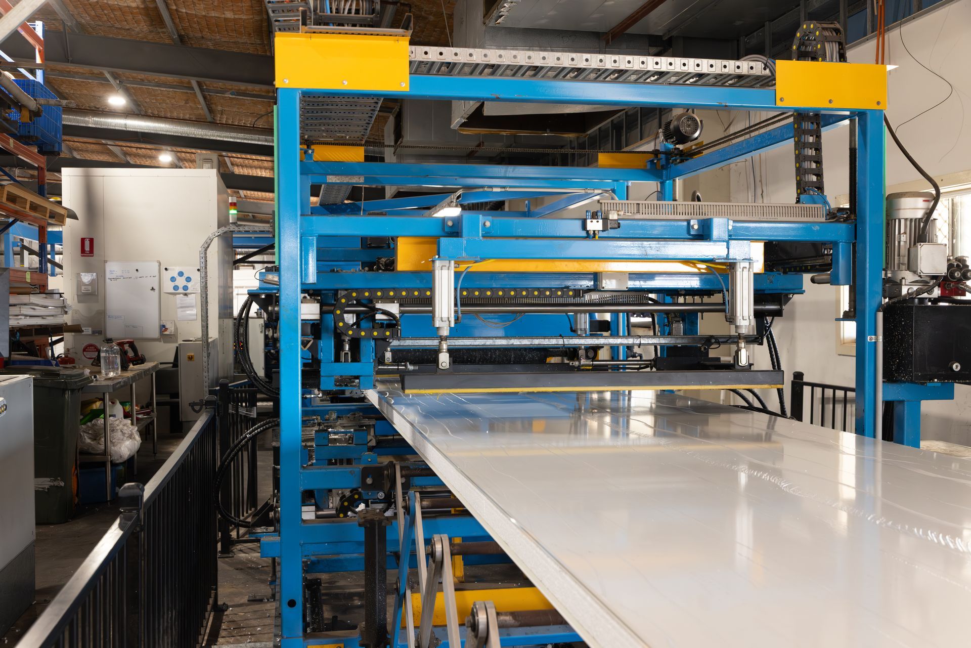 Blue and yellow industrial machine, processing a large white sheet in a factory setting.
