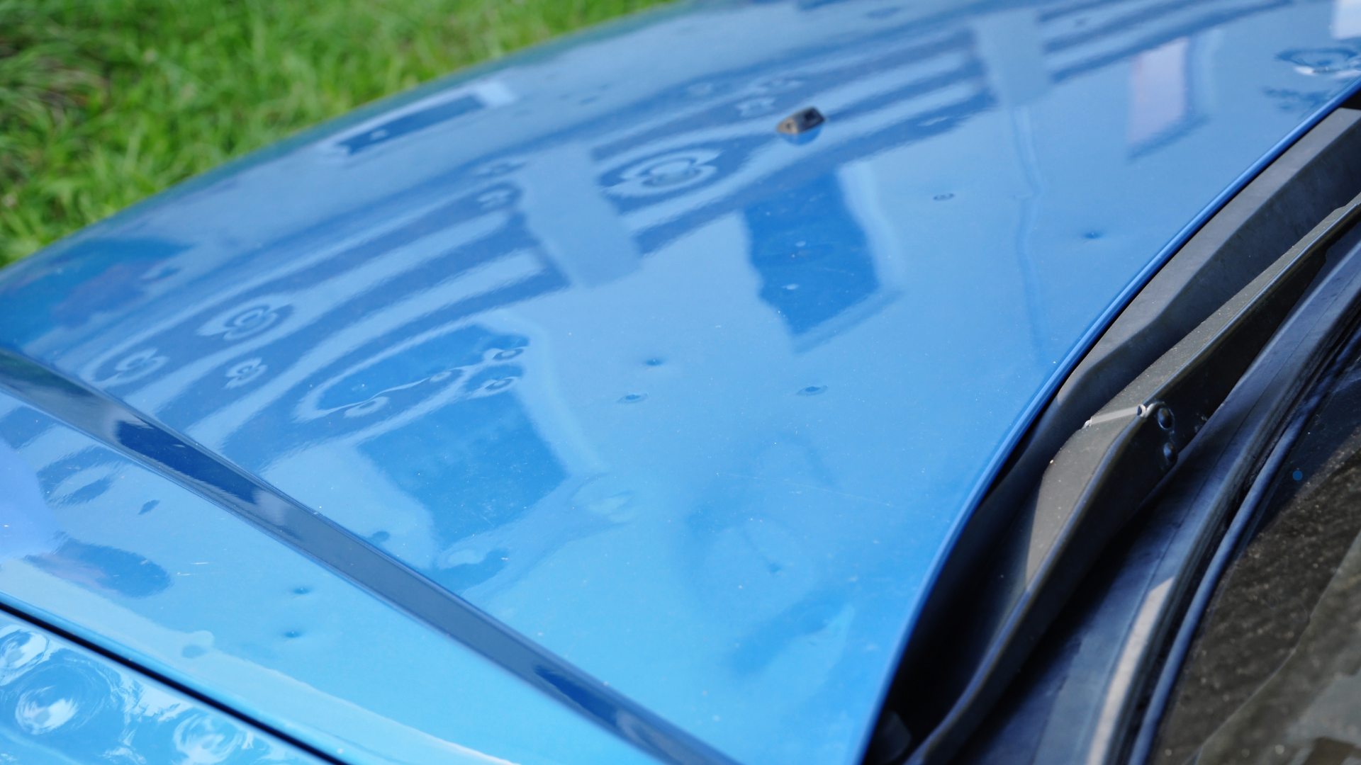 Close-up view of a blue car roof with visible hail damage, showing multiple small dents caused by hailstones.