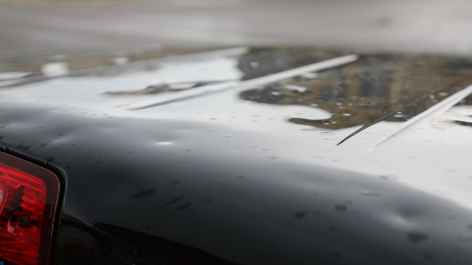 Close-up view of a black car roof with noticeable hail damage, with several dents clearly visible fr