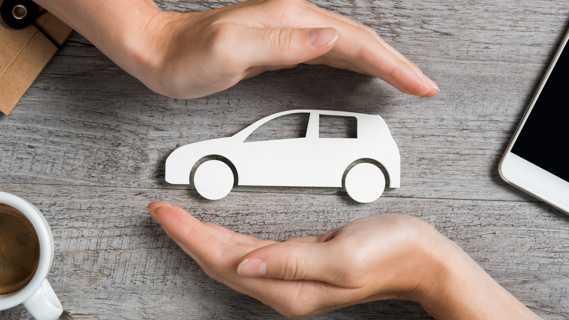 Two hands surrounding a white cut-out model of a car, representing the protection and coverage that