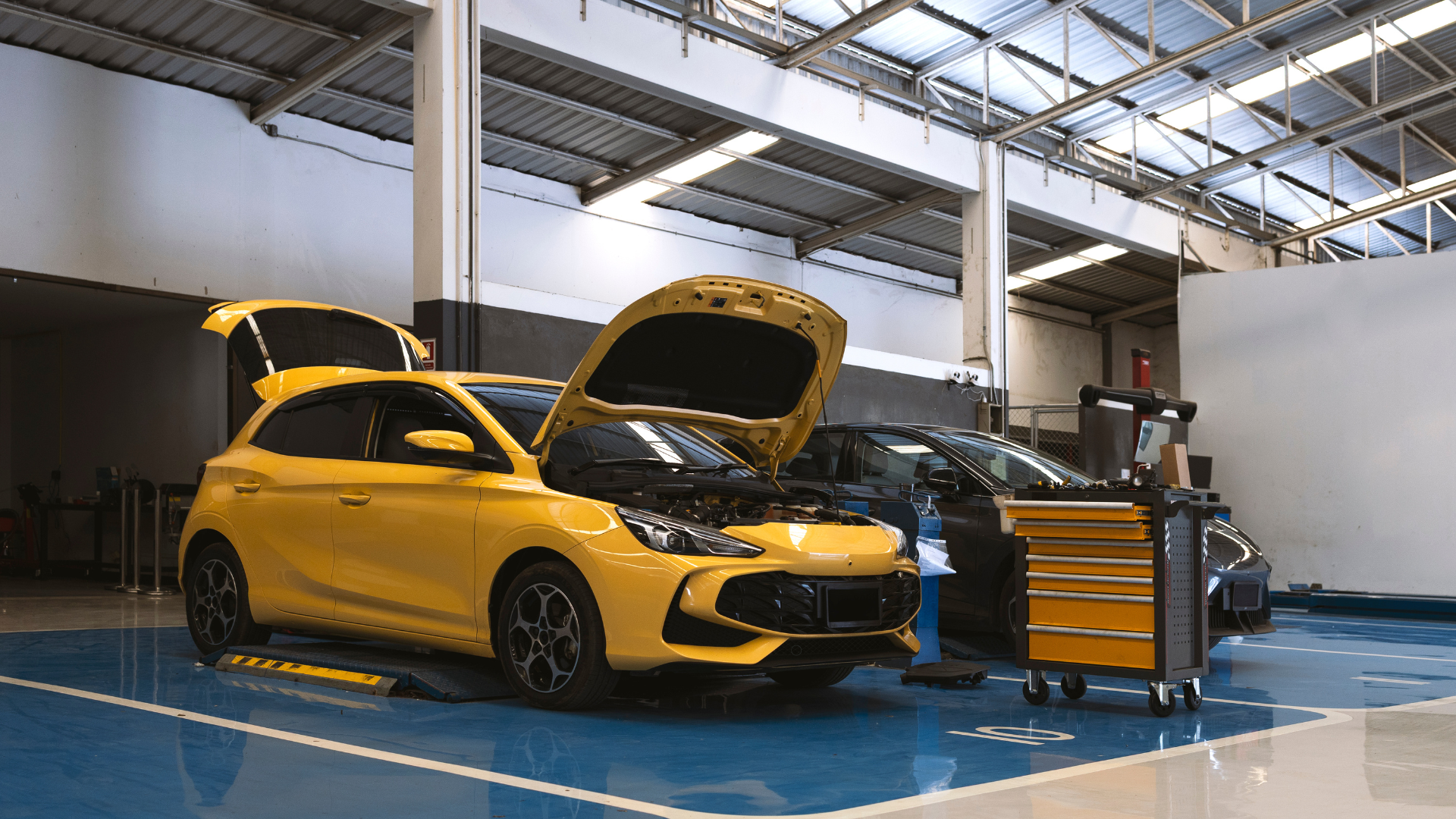 Yellow car in an auto repair shop with the hood open, showcasing the vehicle's engine bay, surrounded by a professional garage setup.