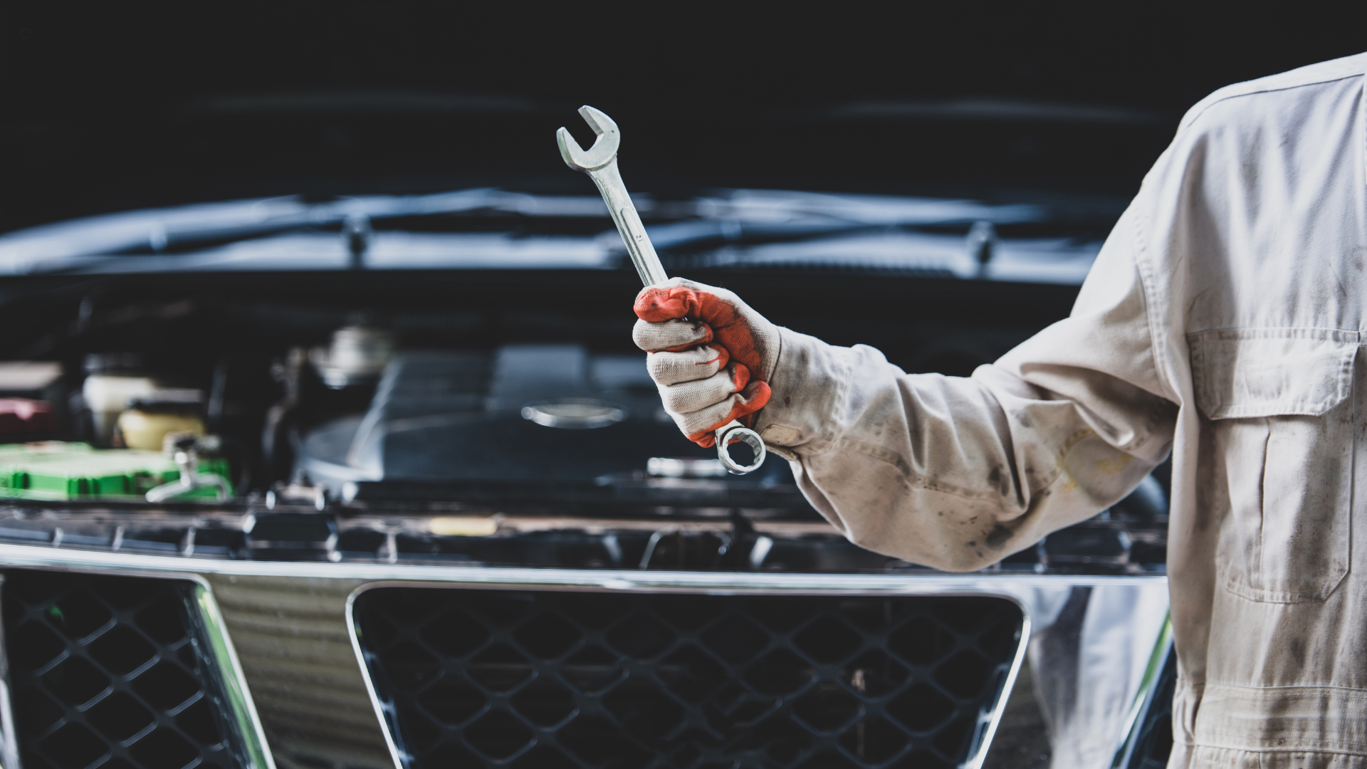 Close-up of a mechanic holding a wrench, standing in front of a car with the hood open, ready to per