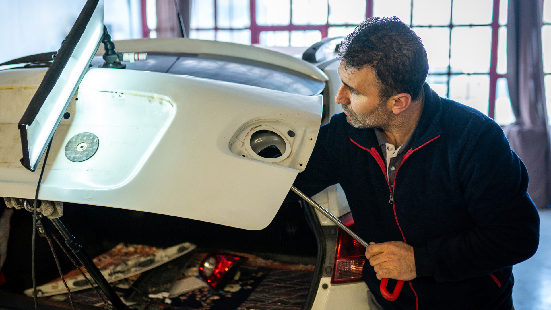 A mechanic inspecting and repairing a car’s rear end with a flashlight in a workshop, focusing on th