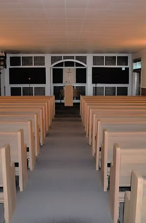 Empty church interior with rows of pews facing a podium and altar; gray carpet and dust.