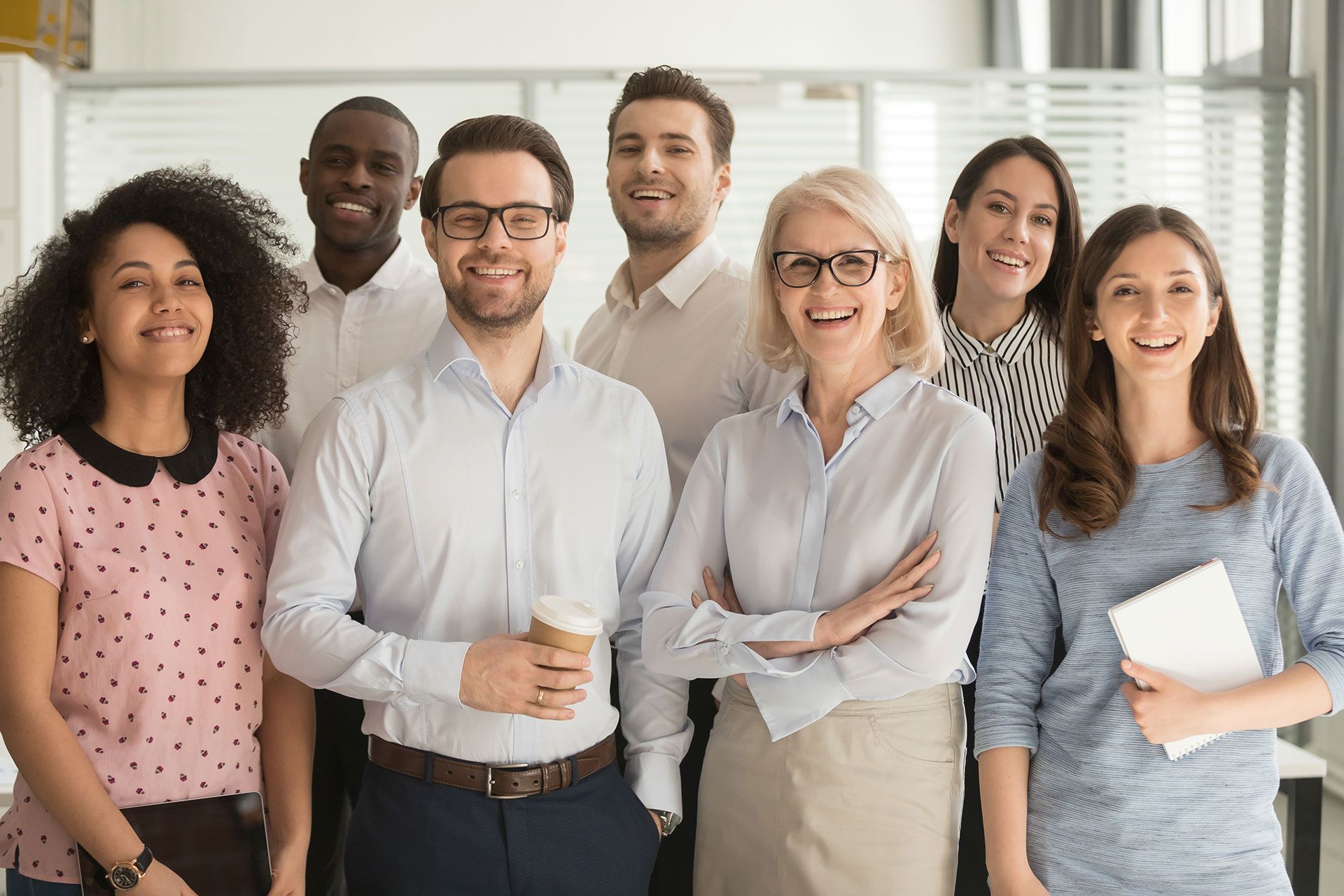 Group of people smiling, looking at the camera, in a bright office.