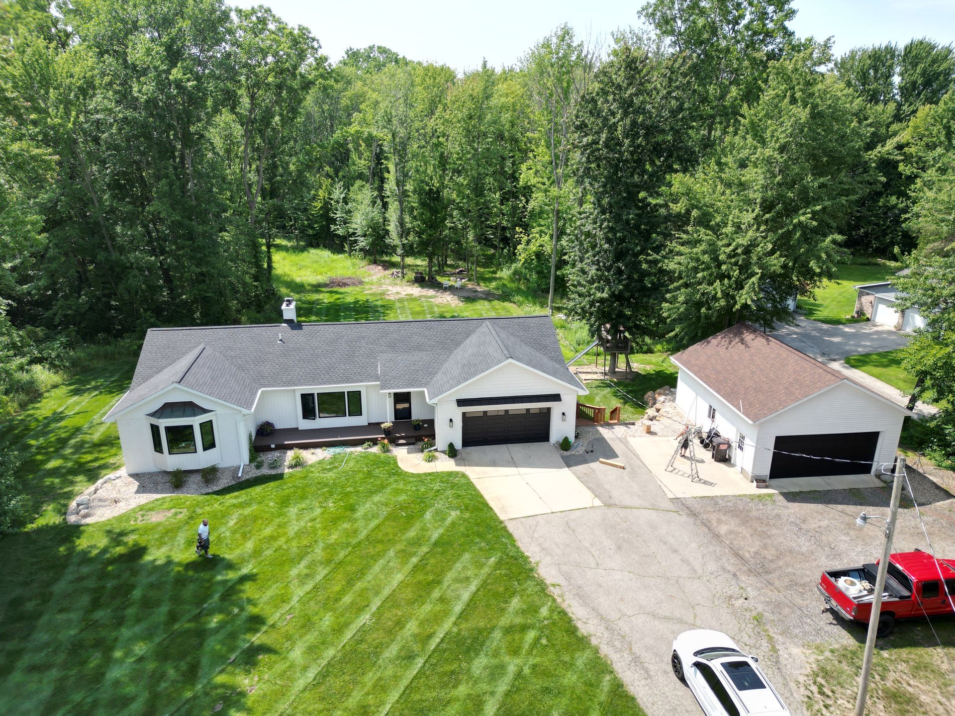 picture of a residential roof completed by top shelf construction and consulting. house is surrounded by a pristine wooded area and diagonal-pattern lawn.