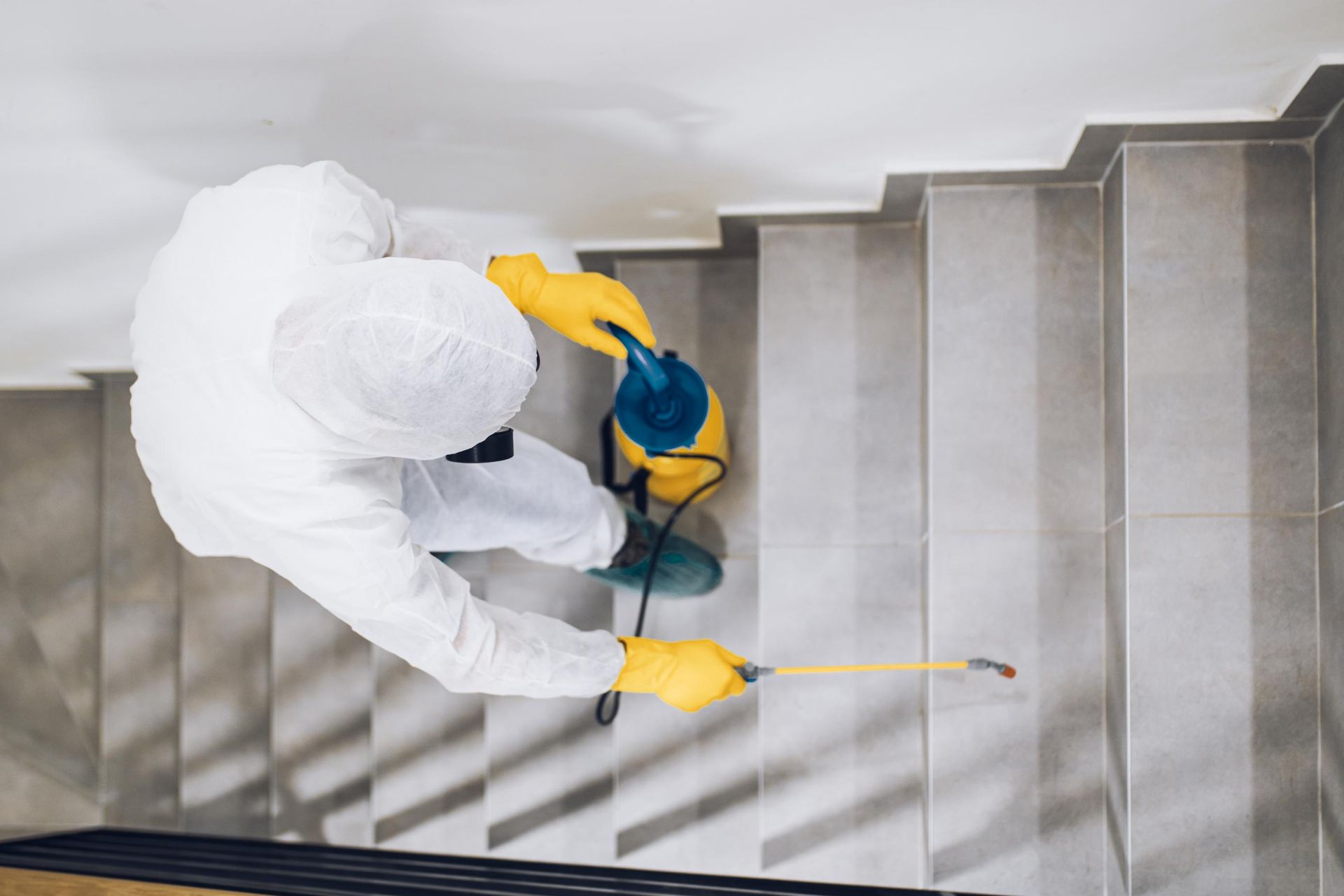 A man in a protective suit is spraying a staircase with a sprayer.