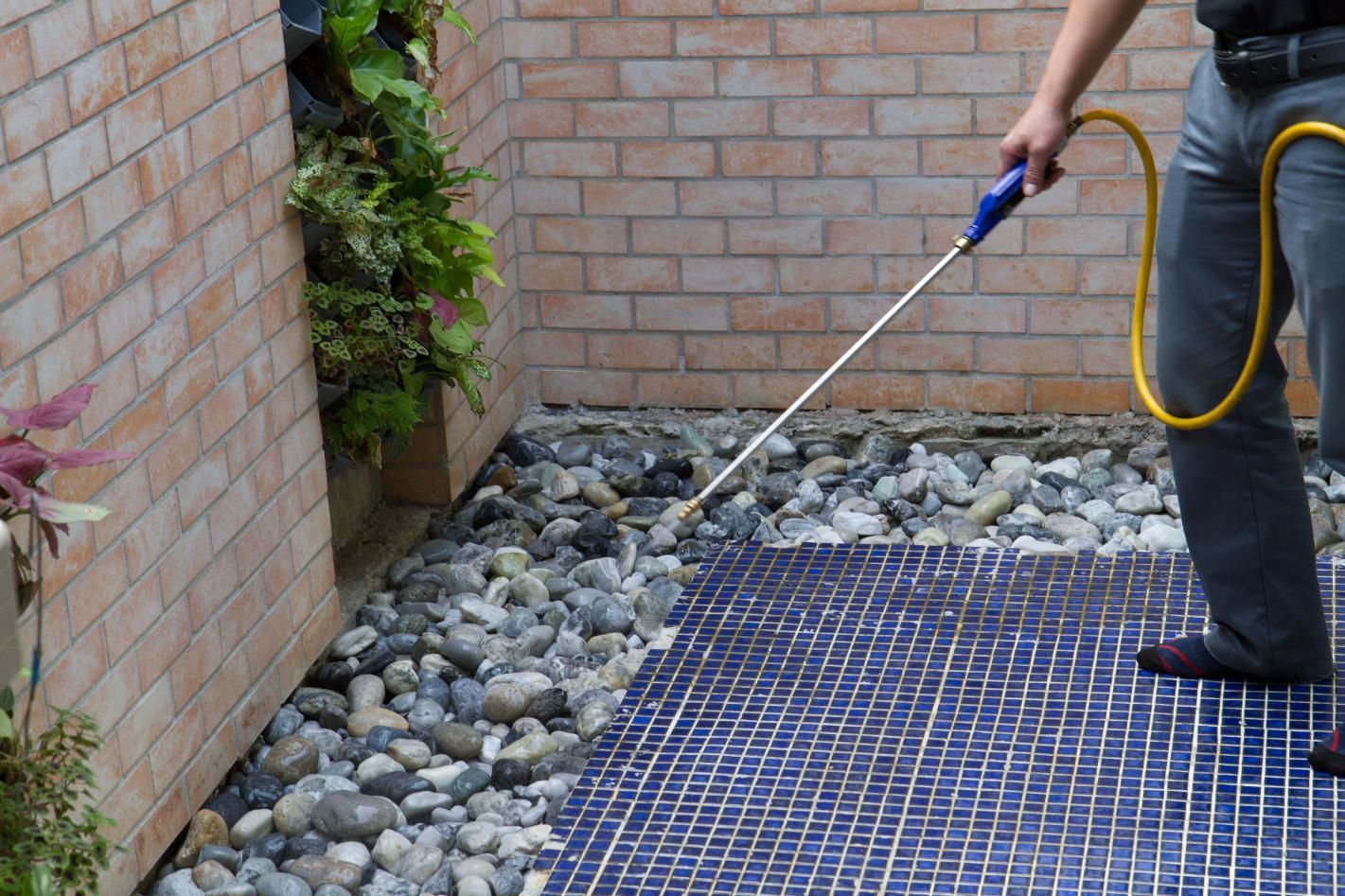 A man is spraying a blue tile floor with a hose.