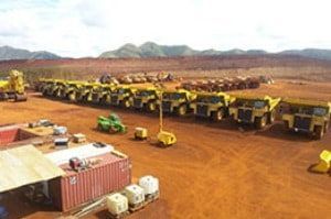 A row of yellow trucks are parked in a dirt field.