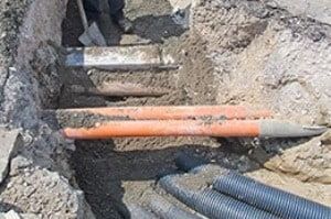 A bunch of pipes are laying in the dirt in a trench.